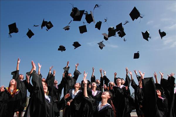 Students in graduation gowns tossing their hats into the blue sky